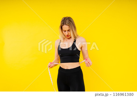 A weight loss and healthy lifestyle concept. Smiling slim woman measuring her waist with tape A weight loss and healthy lifestyle concept. Smiling slim woman measuring her waist with tape 116961380