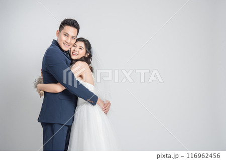 Happy smiling Asian couple in love in wedding dress embracing each other on white background Happy smiling Asian couple in love in wedding dress embracing each other on white background 116962456