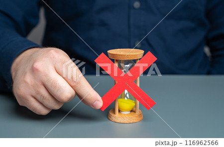 A man holds a red cross on top of an hourglass. End of time. Blocking and prohibition on further work. Refusal of additional time, termination of the contract. A man holds a red cross on top of an hourglass. End of time. Blocking and prohibition on further work. Refusal of additional time, termination of the contract. 116962566