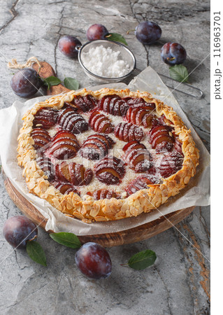 Summer plum galette with almonds and powdered sugar close-up on wooden board. Vertical Summer plum galette with almonds and powdered sugar close-up on wooden board. Vertical 116963701