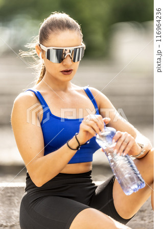Young sporty woman drinking water from a bottle after exercising at the park 116964236