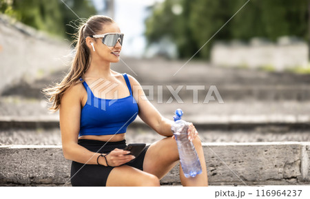 Young sporty woman drinking water from a bottle after exercising at the park 116964237