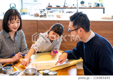 防災用品が並べられたつくテーブルを囲んでの家族会議でケミカルライトに興味を示す女の子 116965845