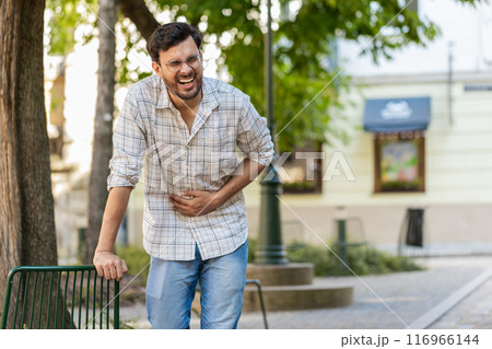 Indian young man traveler feeling sudden strong abdominal stomach ache, gastritis problem on street 116966144