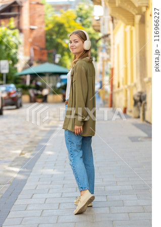 Happy young woman in wireless headphones listening favorite energetic disco music dancing outdoors 116966227