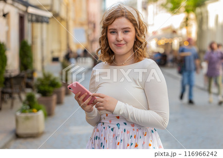 Young woman use smartphone typing text messages browsing internet finishing work looking at camera Young woman use smartphone typing text messages browsing internet finishing work looking at camera 116966242