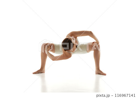 Athletic woman deepens her flexibility and balance through wide-legged squat, practicing yoga against white studio background. 116967141
