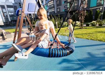 Mother Joyfully Interacting With Her Two Sons on a Vibrant Playground in Afternoon Sunshine 116967814
