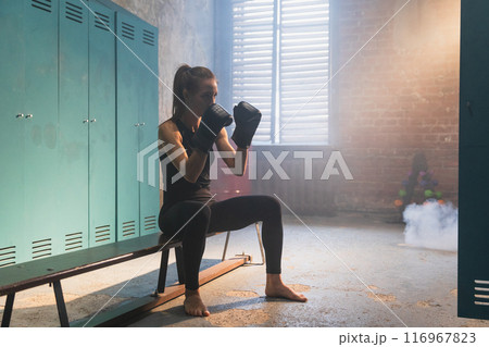 Workout in gym. Woman fighter ready for fight punching with boxing gloves in locker room. Strong girl training punches preparing for boxing sparring active exercise workout training in gym 116967823