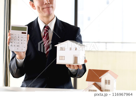 住宅模型と電卓を持ち悩むスーツ姿のアジア人男性のビジネスパーソン 住宅模型と電卓を持ち悩むスーツ姿のアジア人男性のビジネスパーソン 116967964