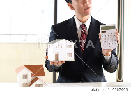 住宅模型と電卓を持ち悩むスーツ姿のアジア人男性のビジネスパーソン 116967966