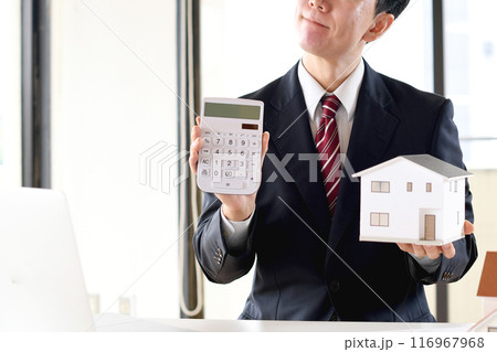 住宅模型と電卓を持ち悩むスーツ姿のアジア人男性のビジネスパーソン 116967968