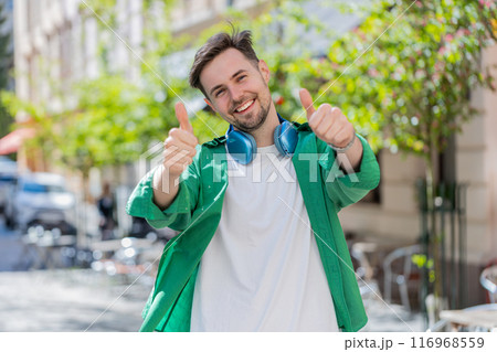 Happy man tourist showing thumbs up like positive something good positive feedback on city street Happy man tourist showing thumbs up like positive something good positive feedback on city street 116968559