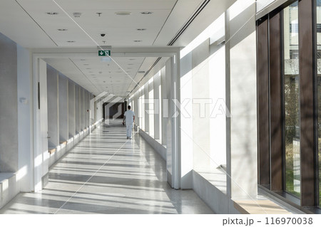 A medical worker walks along a long white corridor in a hospital A medical worker walks along a long white corridor in a hospital 116970038