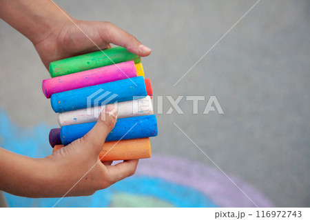 Chalks. Large colored crayons in children's hands. The child holds the chalk. Draw on the street. Chalks. Large colored crayons in children's hands. The child holds the chalk. Draw on the street. 116972743