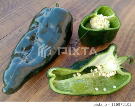 木目のテーブルに並べたメキシコの唐辛子　チレ・ポブラーノ1本、縦切り、横切り　 116973102