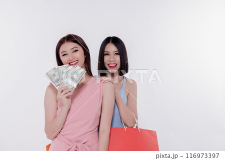 Two smiling women shopping with bags, enjoying a day out, She is holding a dollar bill on a white background. Two smiling women shopping with bags, enjoying a day out, She is holding a dollar bill on a white background. 116973397