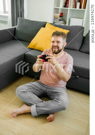 Man playing video games in living room sitting on sofa. 116974270