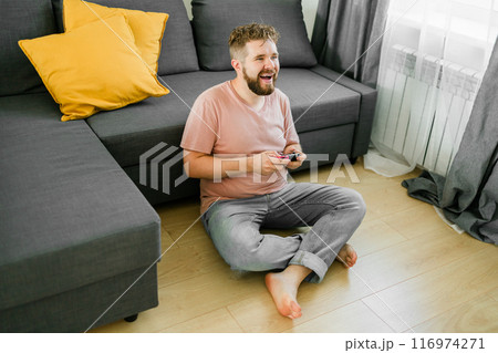 Man playing video games in living room sitting on sofa. 116974271