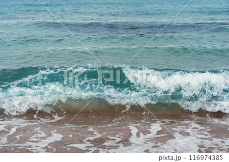 A refreshing wave crashes on a sandy beach, showcasing the 116974385