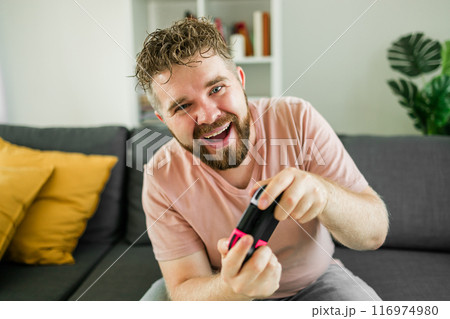 Man playing video games in living room sitting on sofa. Man playing video games in living room sitting on sofa. 116974980