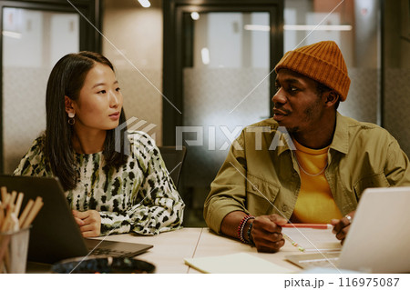 Young African American designer and Asian manager working together on new project while sitting at desk in modern office 116975087