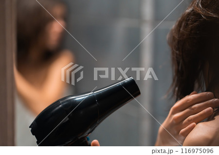 Girl is using hairdryer near the mirror, closeup. 116975096
