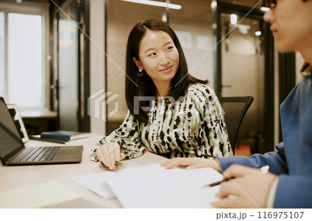 Young Asian manager sitting at desk and looking at her male colleague while working with documents together 116975107