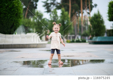 Toddler girl jumping through puddles in summer Toddler girl jumping through puddles in summer 116975285