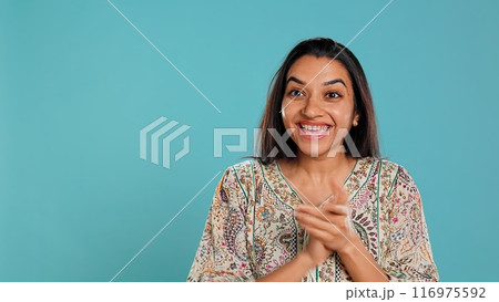 Joyful indian woman happily clapping hands, ecstatic about accomplishments. Excited person reacting to good news, cheering, applauding, isolated over studio background, camera B 116975592