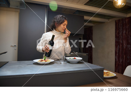 Woman enjoying pasta meal with red wine in modern kitchen 116975660