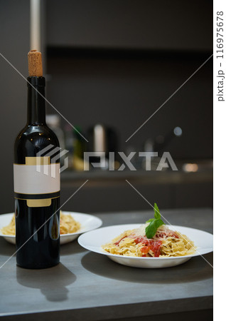 Elegant dinner setup with bottle of wine and pasta plates in a modern kitchen Elegant dinner setup with bottle of wine and pasta plates in a modern kitchen 116975678