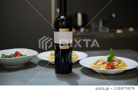Elegant dinner setting with wine bottle and pasta dishes in a modern kitchen 116975679