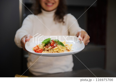 Smiling woman presenting a delicious plate of pasta with fresh tomatoes and basil 116975700