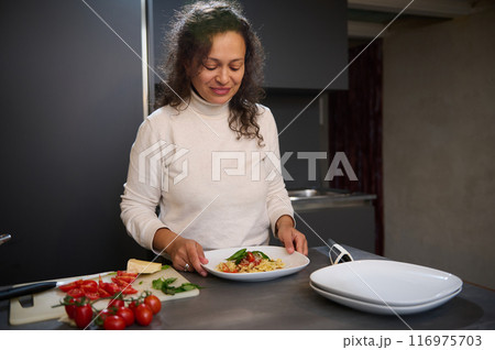 Woman preparing a delicious pasta dish in modern kitchen with fresh tomatoes and basil 116975703