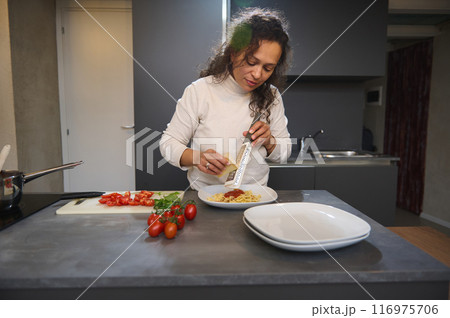 Woman preparing a fresh pasta dish with grated cheese and tomatoes in modern kitchen 116975706