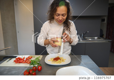 Woman grating cheese over pasta in a modern kitchen preparing an Italian meal 116975707
