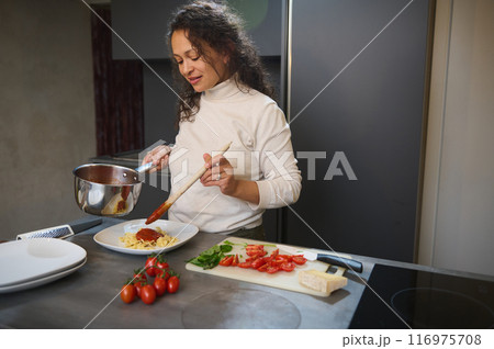 Woman cooking pasta with tomato sauce in a modern kitchen 116975708