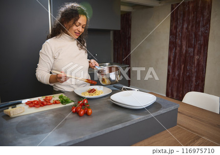 Woman cooking fresh pasta in modern kitchen, adding tomato sauce to plate 116975710