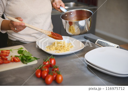 Preparing pasta with tomato sauce in a kitchen, ingredients include fresh tomatoes and basil 116975712