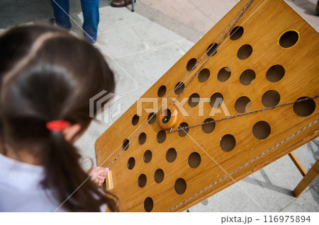 Child playing a wooden marble maze game at an outdoor event 116975894