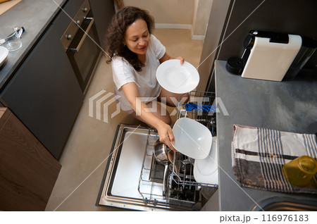 Smiling woman loading dishwasher in modern kitchen, doing house chores Smiling woman loading dishwasher in modern kitchen, doing house chores 116976183