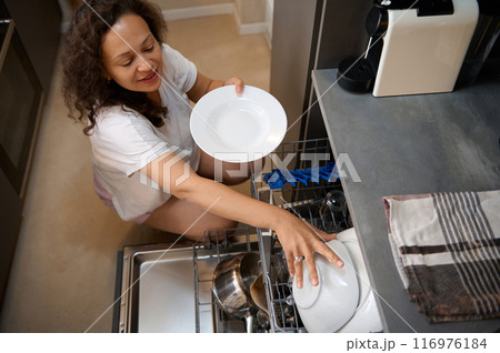 Woman loading dishes into dishwasher in modern kitchen, doing daily household chores Woman loading dishes into dishwasher in modern kitchen, doing daily household chores 116976184