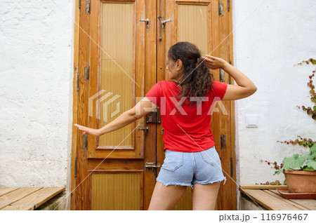 Woman dancing joyfully in front of a wooden door, wearing red shirt and denim shorts Woman dancing joyfully in front of a wooden door, wearing red shirt and denim shorts 116976467