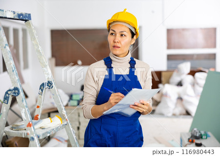 Woman worker checking documents during repair works indoors 116980443