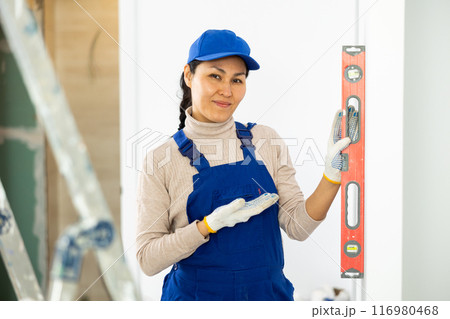 Woman builder using building level measures the vertical of wall Woman builder using building level measures the vertical of wall 116980468