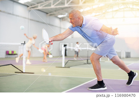 Sporty senior man playing pickleball on indoor court 116980470