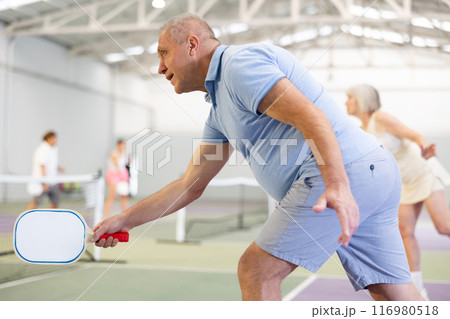 Sporty senior man playing pickleball on indoor court Sporty senior man playing pickleball on indoor court 116980518