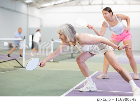 Positive elderly woman playing pickleball on indoor court Positive elderly woman playing pickleball on indoor court 116980548