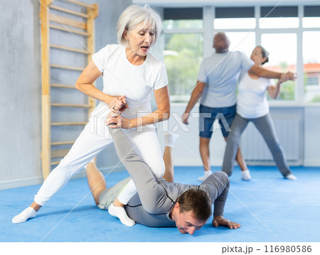 Senior woman in pair with middle-aged coach train Krav Maga and self-defense skills. Senior woman in pair with middle-aged coach train Krav Maga and self-defense skills. 116980586